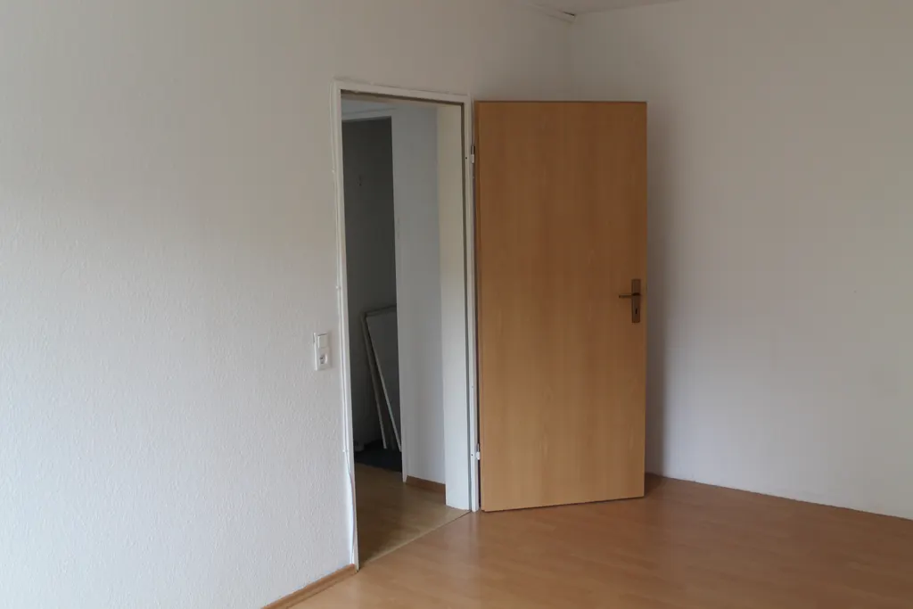 Helles Zimmer mit Holzboden und Tür zum Flur
